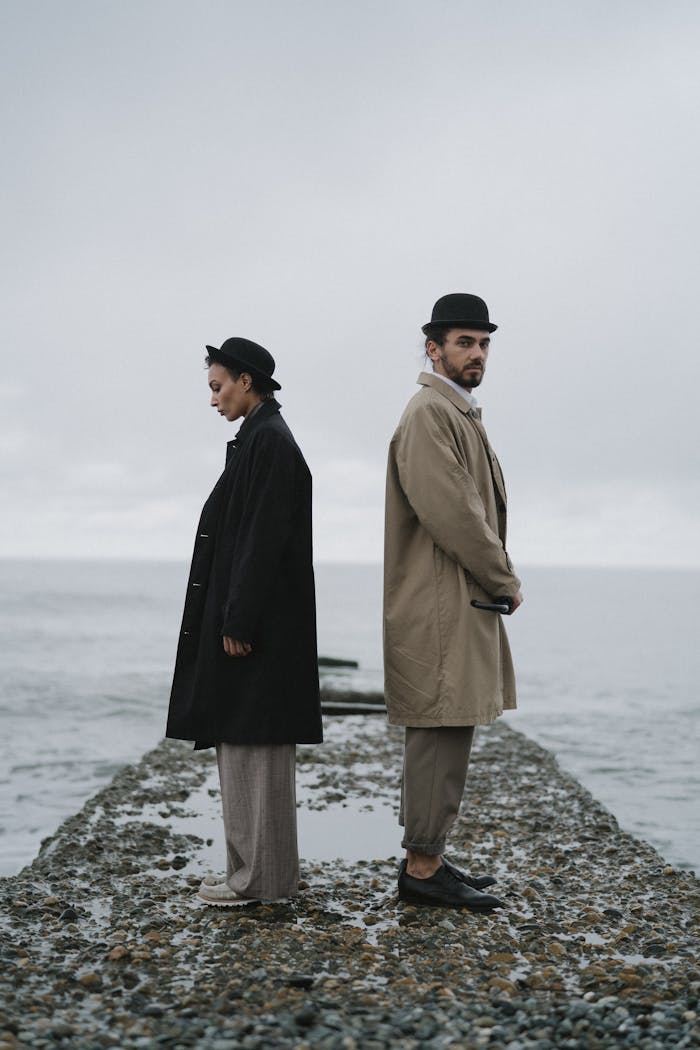 Couple standing back-to-back on a rocky pier by the sea, evoking themes of isolation and contemplation.